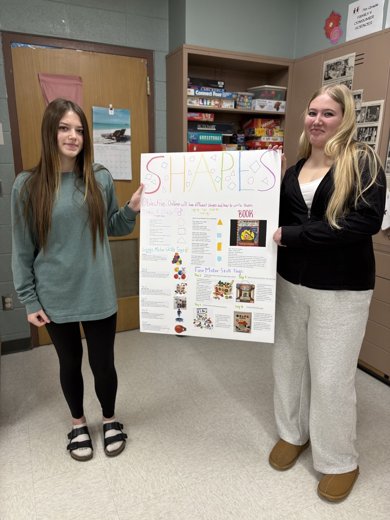 Two high school students hold a poster detailing their lesson plan about shapes.
