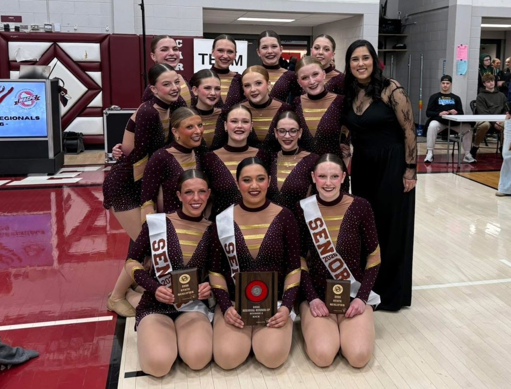 Group of high school dance team members huddle together, smiling.