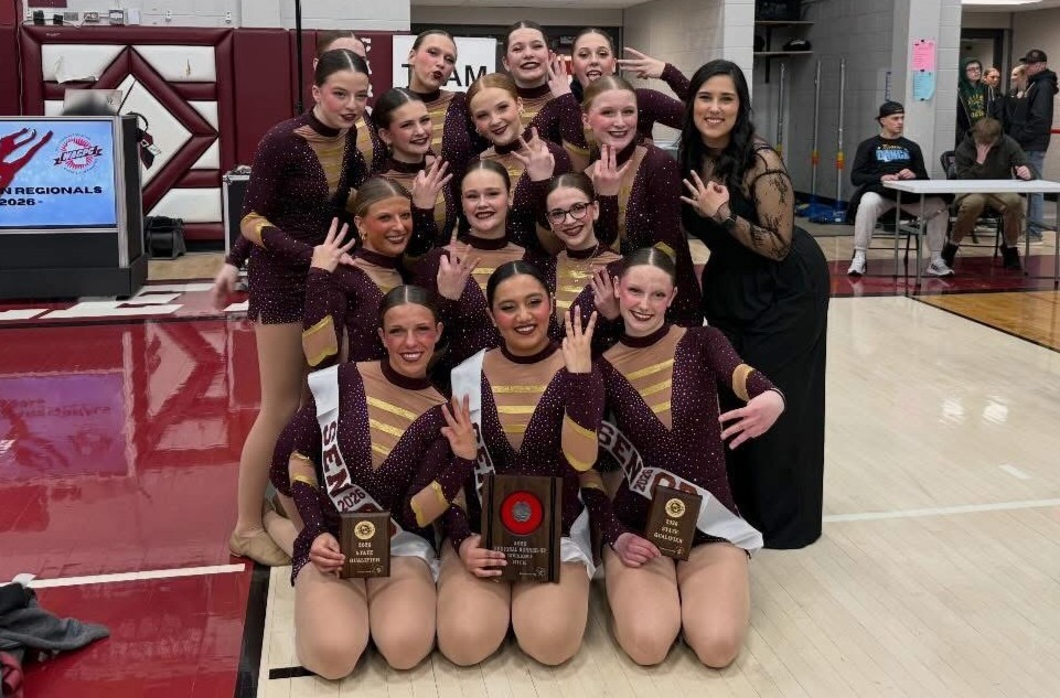 Group of high school dance team members huddle together, smiling.