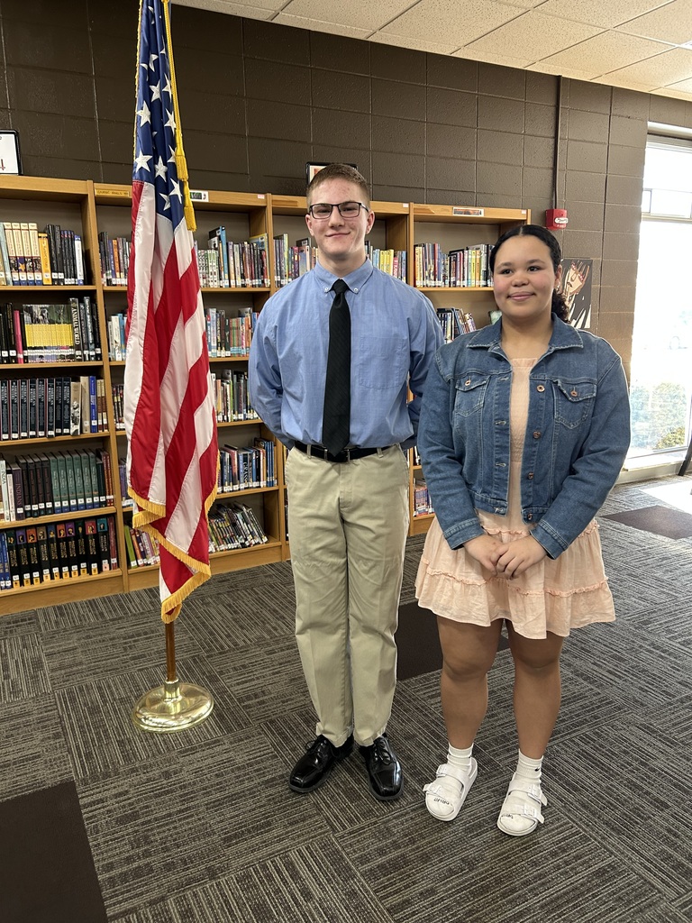 Two high school students standing near a flag.