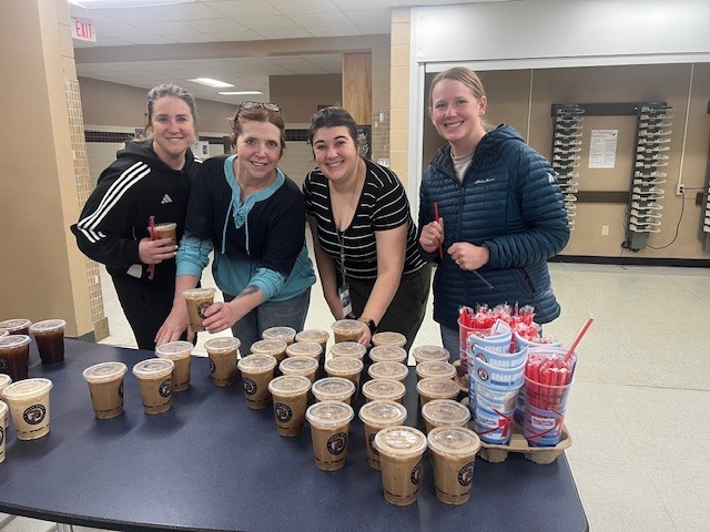 Four adults standing around a table filled with multiple cups of coffee