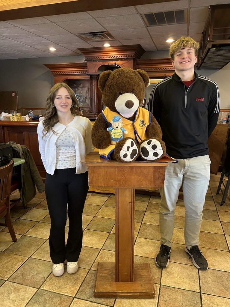 Two high school students standing near a stuffed animal bear.