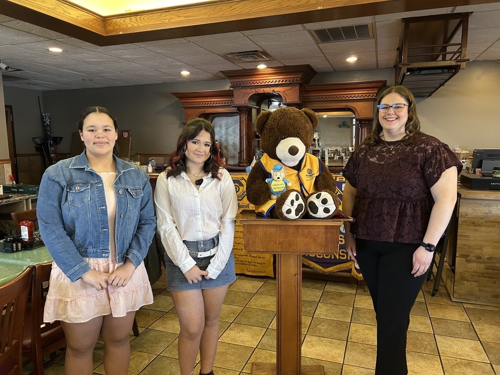 3 high school students standing near a stuffed animal bear.