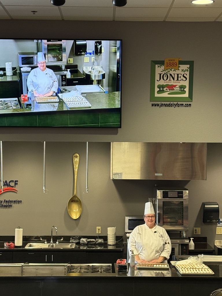 A chef in a kitchen. The chef is also beinig projected on a screen up above.