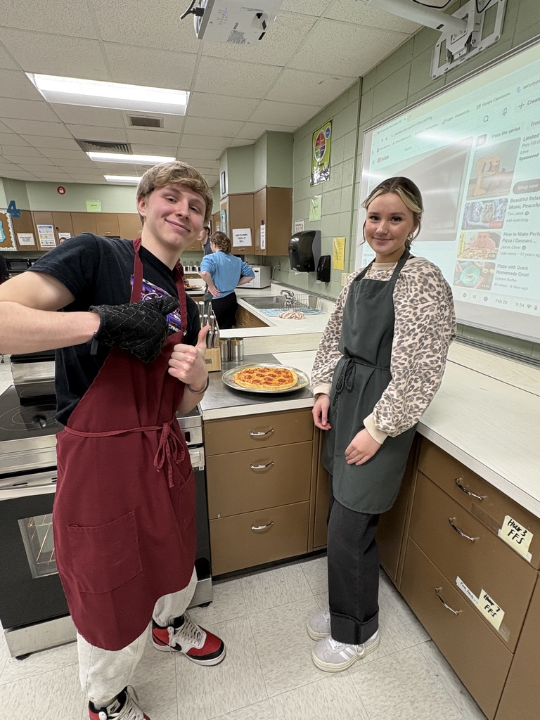 Two high school students standing near a pizza that they made.