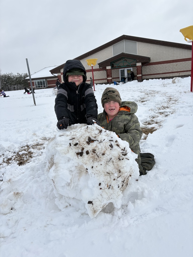 Two elementary school students rolling a large snowball together.