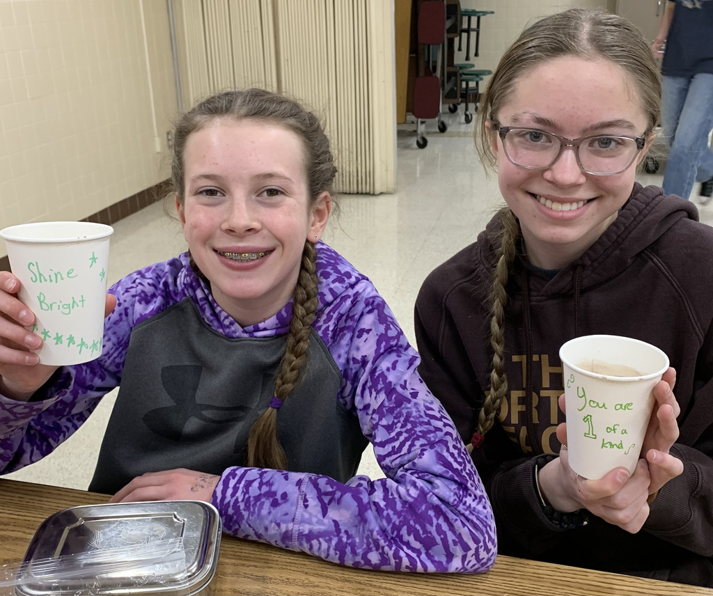 Two middle school girls holding a cup with a positive message on it. 