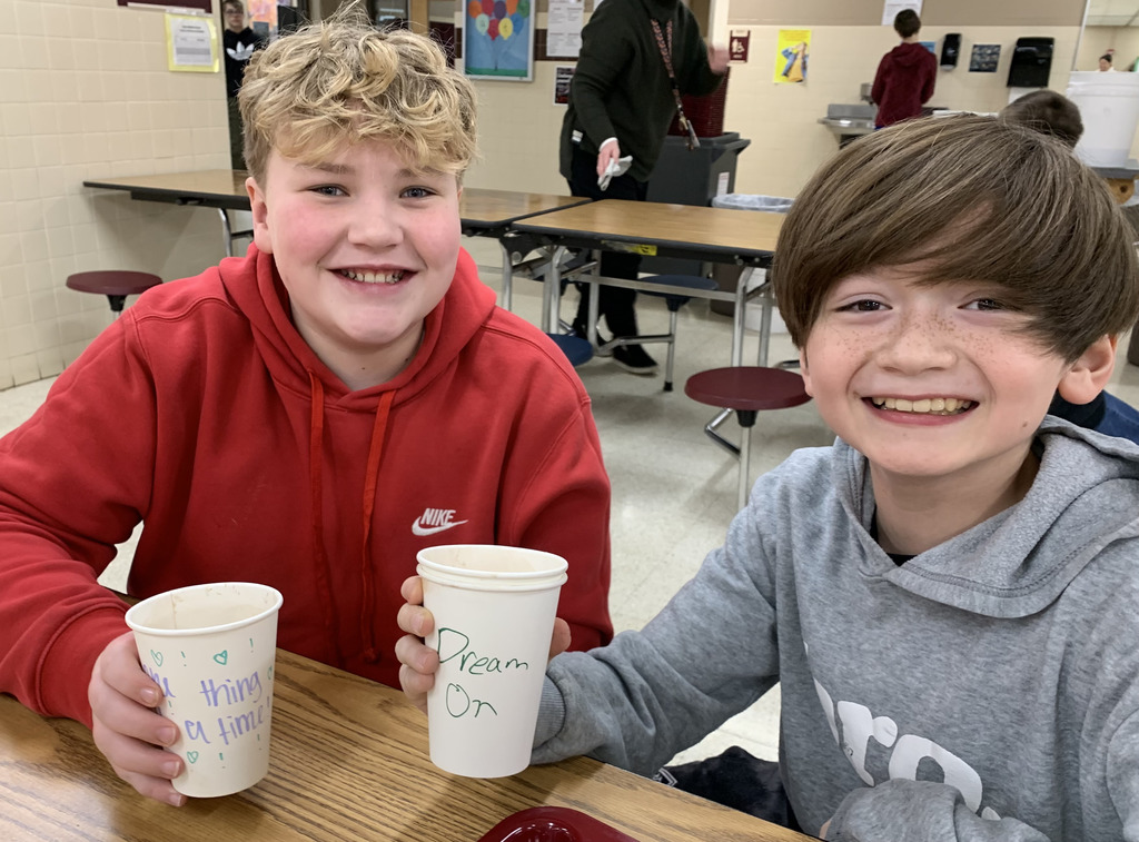 Two middle school boys holding a cup with a positive message on it. 