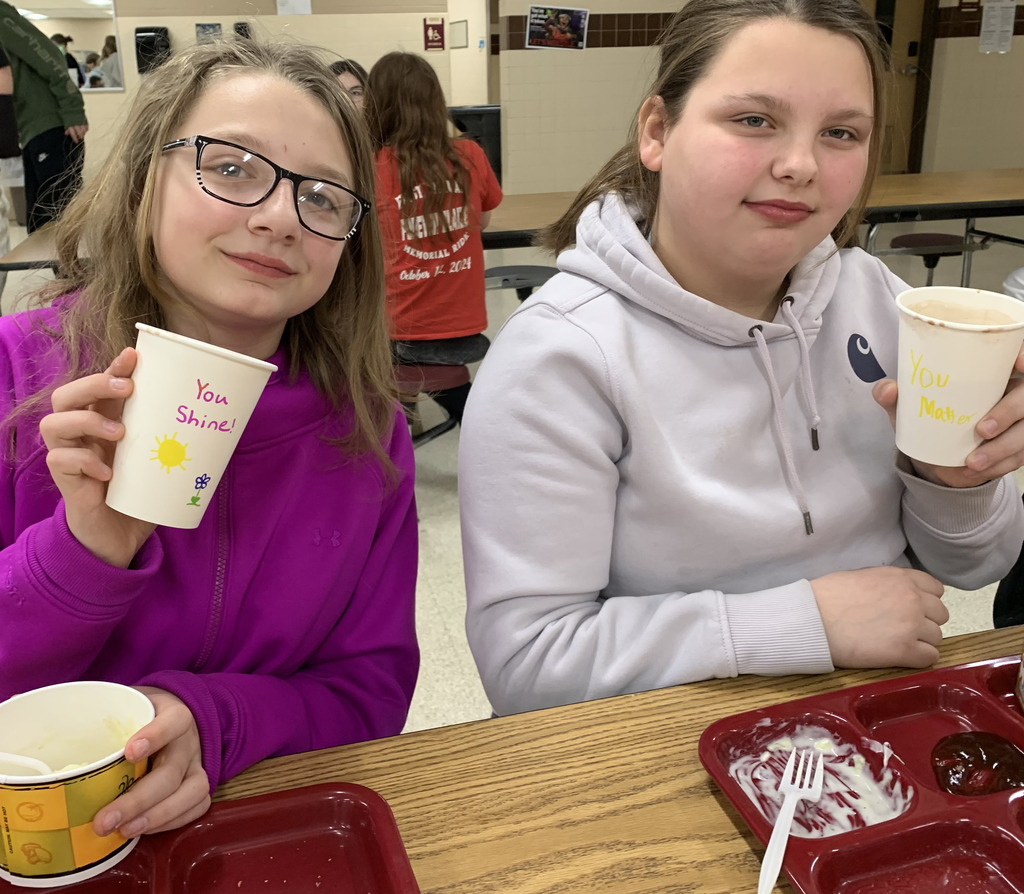 Two middle school girls holding a cup with a positive message on it.