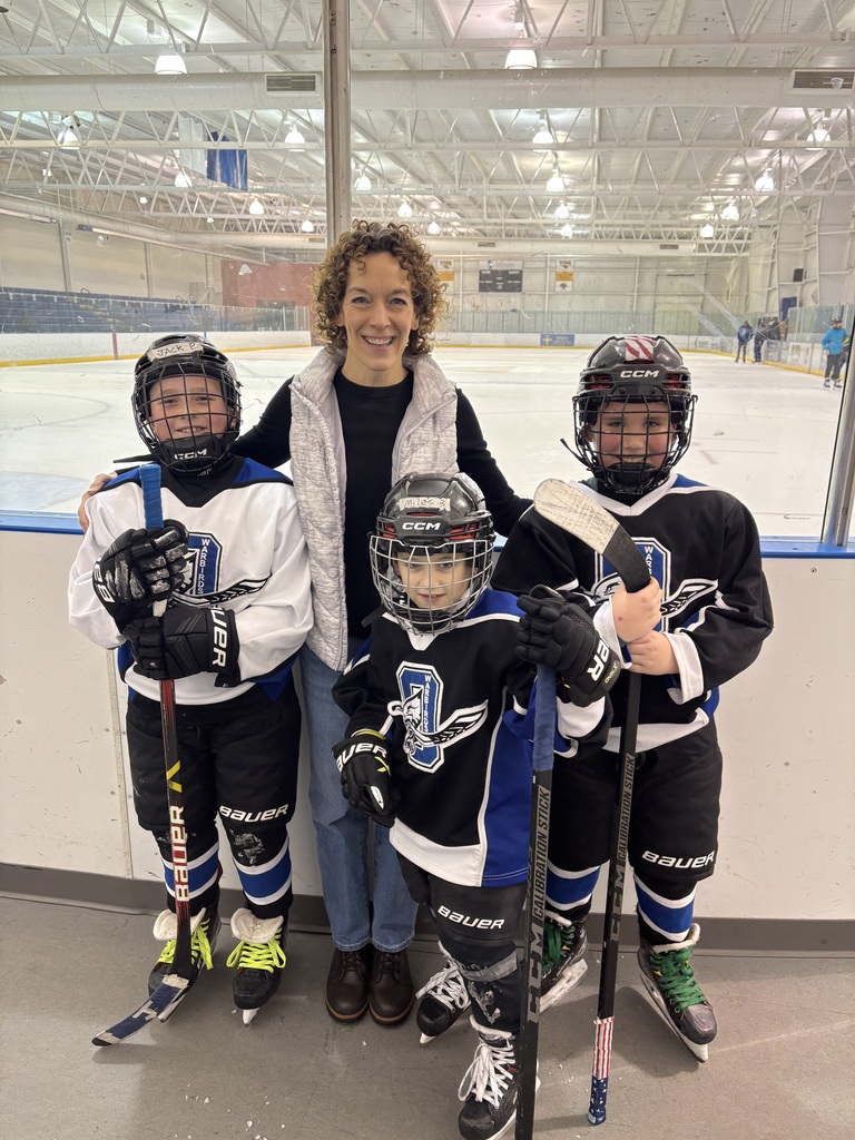 A teacher and three elementary students, wearing hockey gear, standing together.