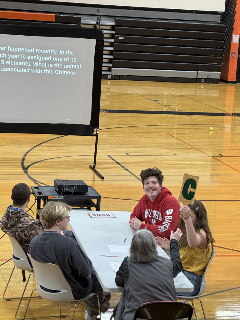 Four high school students sitting at a table, collaborating, with an adult facilitator present.
