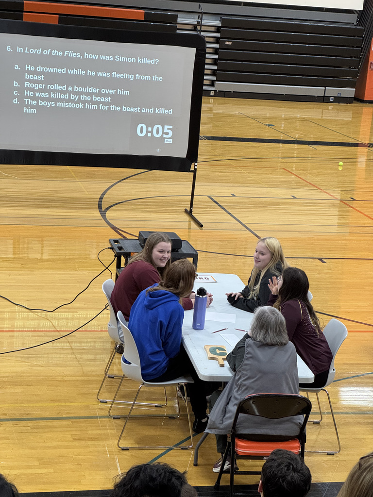 Four high school students sitting at a table, collaborating, with an adult facilitator present.