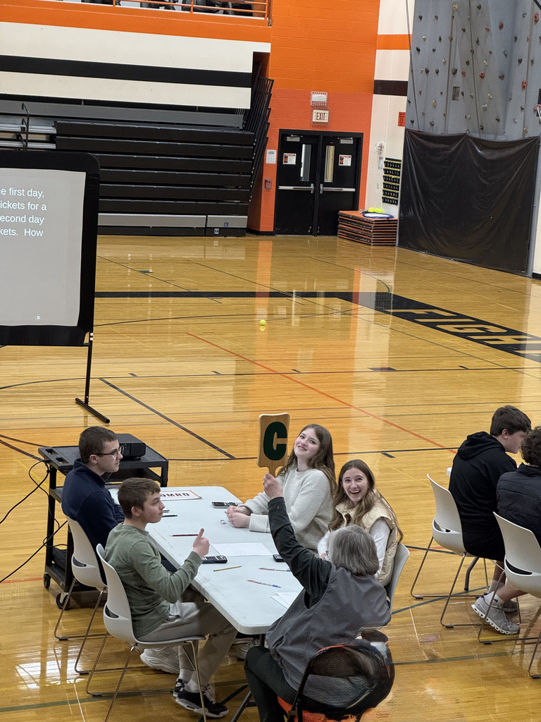 Four high school students sitting at a table, collaborating, with an adult facilitator present.