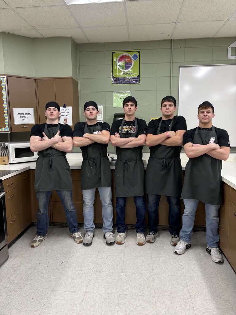 Five high school students wearing black t-shirts, standing in a line in a kitchen.