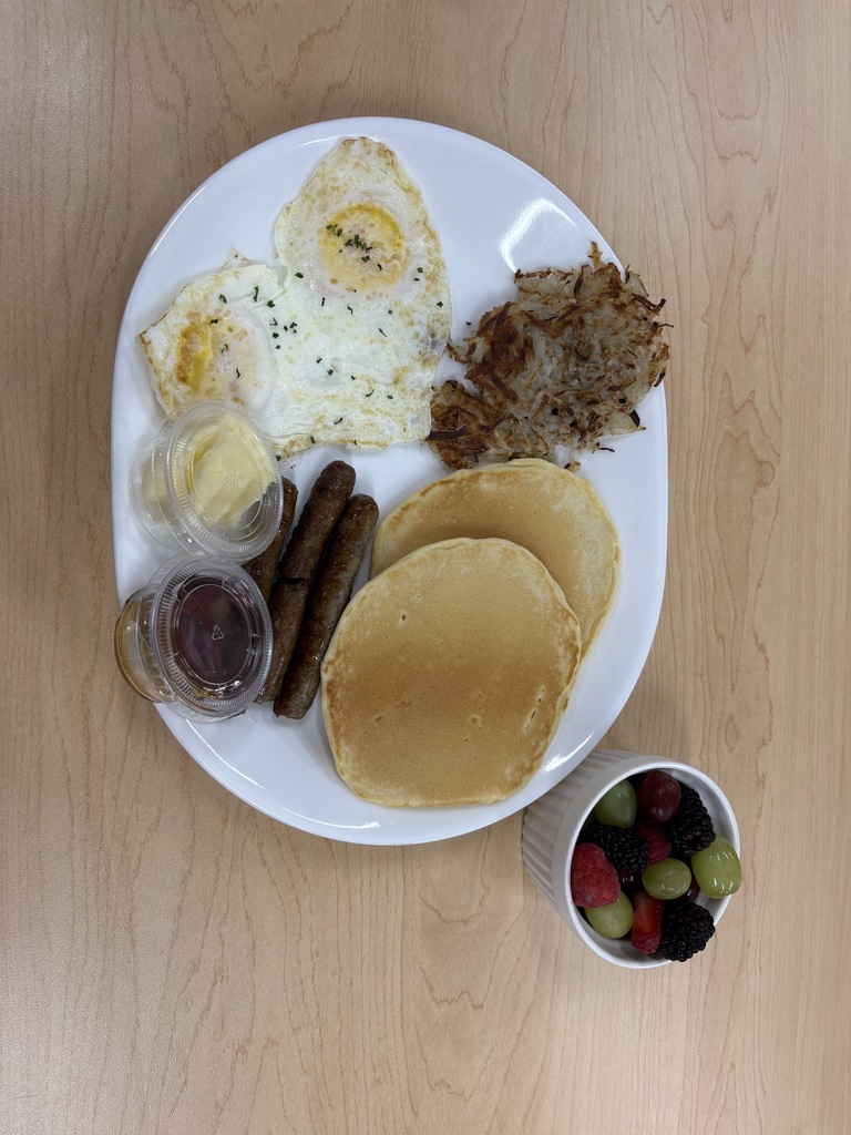 Plate of sausage, pancadkes, eggs, hashbrowns, and fruit.