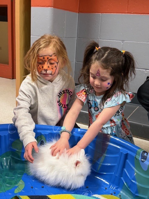 Two young elementary school students petting a rabbit. 