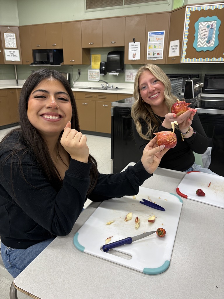 Two high school students showing off their apple birds with cutting board and materials in front of them on a table. 
