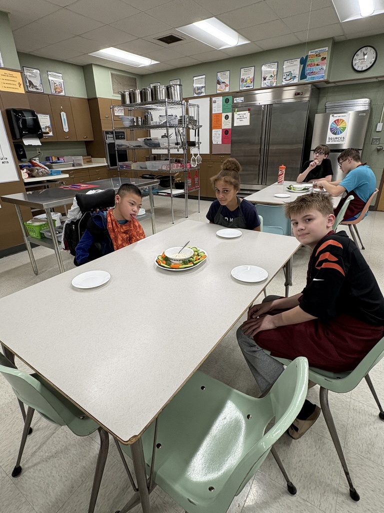 Middle school students sitting at tables with plates of vegetables and dip in front of them. 
