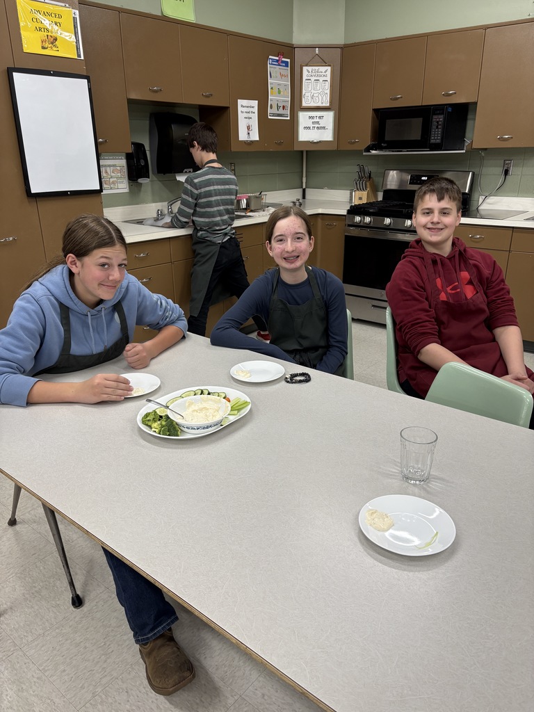 Middle school students sitting at a table with plates of vegetables and dip in front of them. 