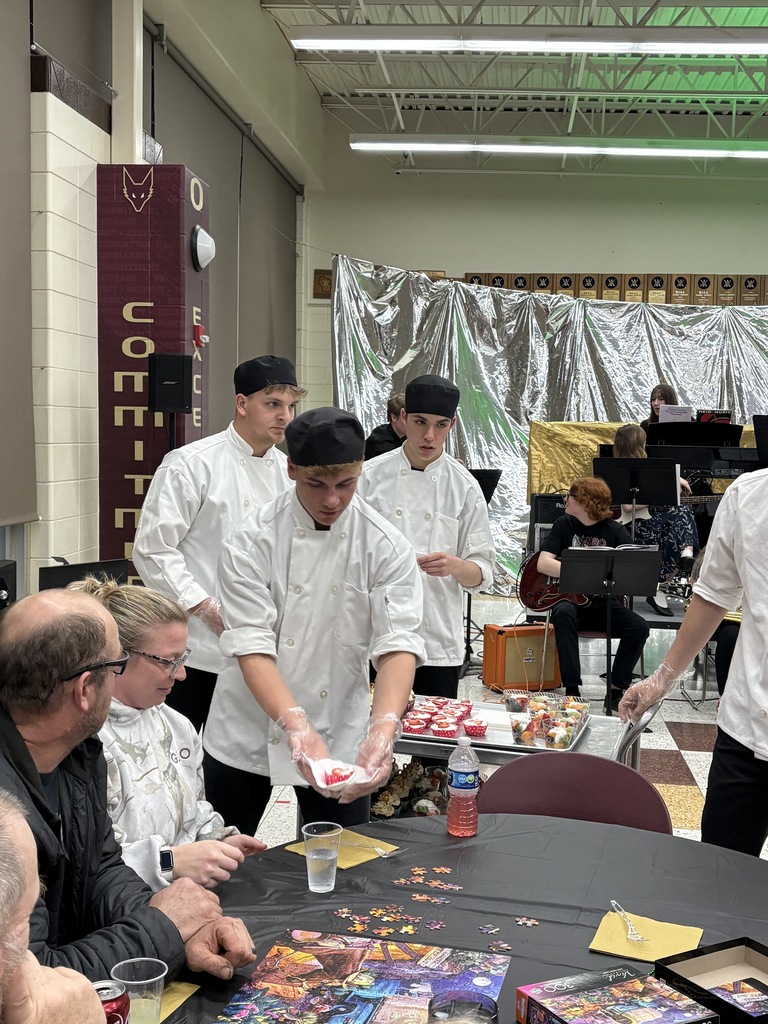 3 high school students serving desserts to adults sitting at a table. 