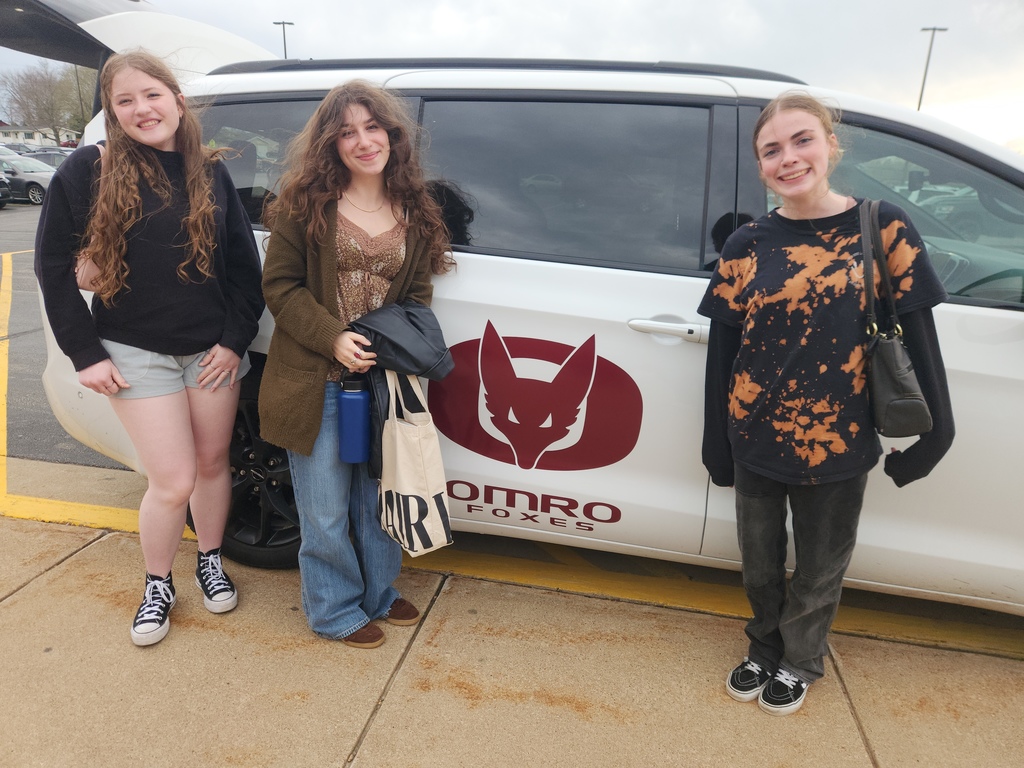 Three high school students pictured with a school van behind them. 