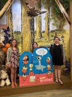 Three elementary students standing behind a sign.