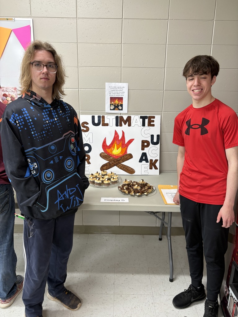 Two high school students standing in front of a poster presentation along with cupcakes on a platter.