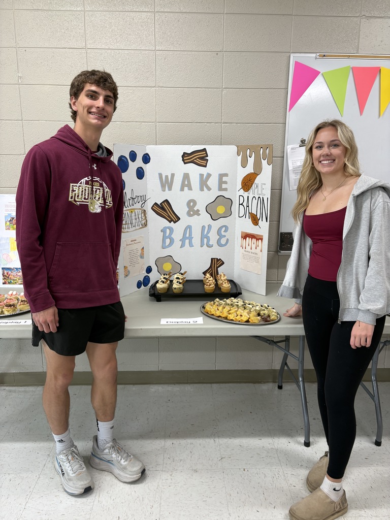 Two high school students standing in front of a poster presentation along with cupcakes.