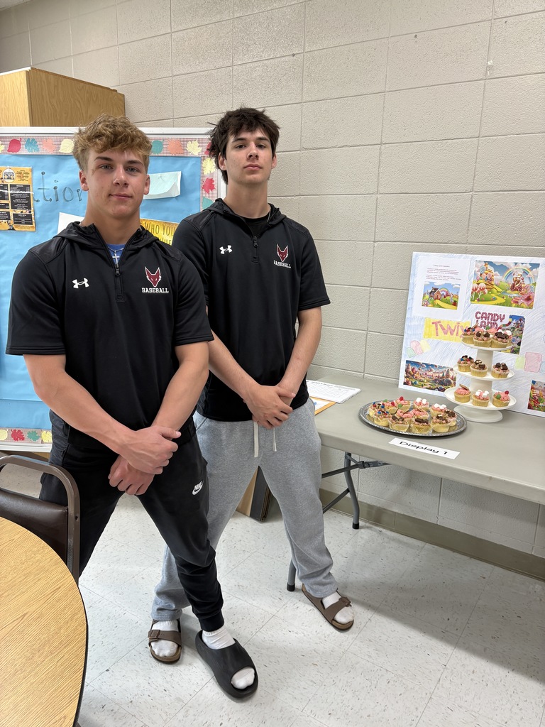 Two high school students standing in front of a poster presentation along with cupcakes on a platter.