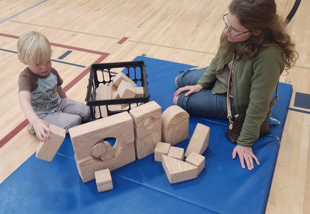 A woman and an early elementary aged student sitting on the floor building with blocks. 