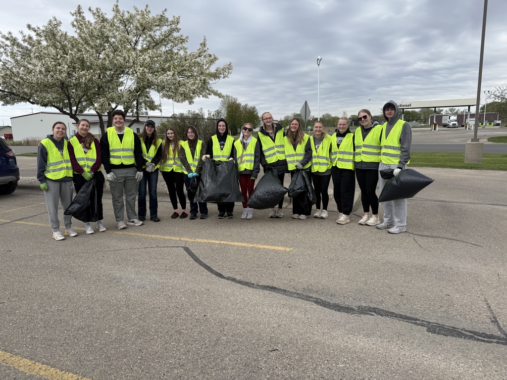 Group of high school students standing in a line holding trash bags and wearing bright vests.