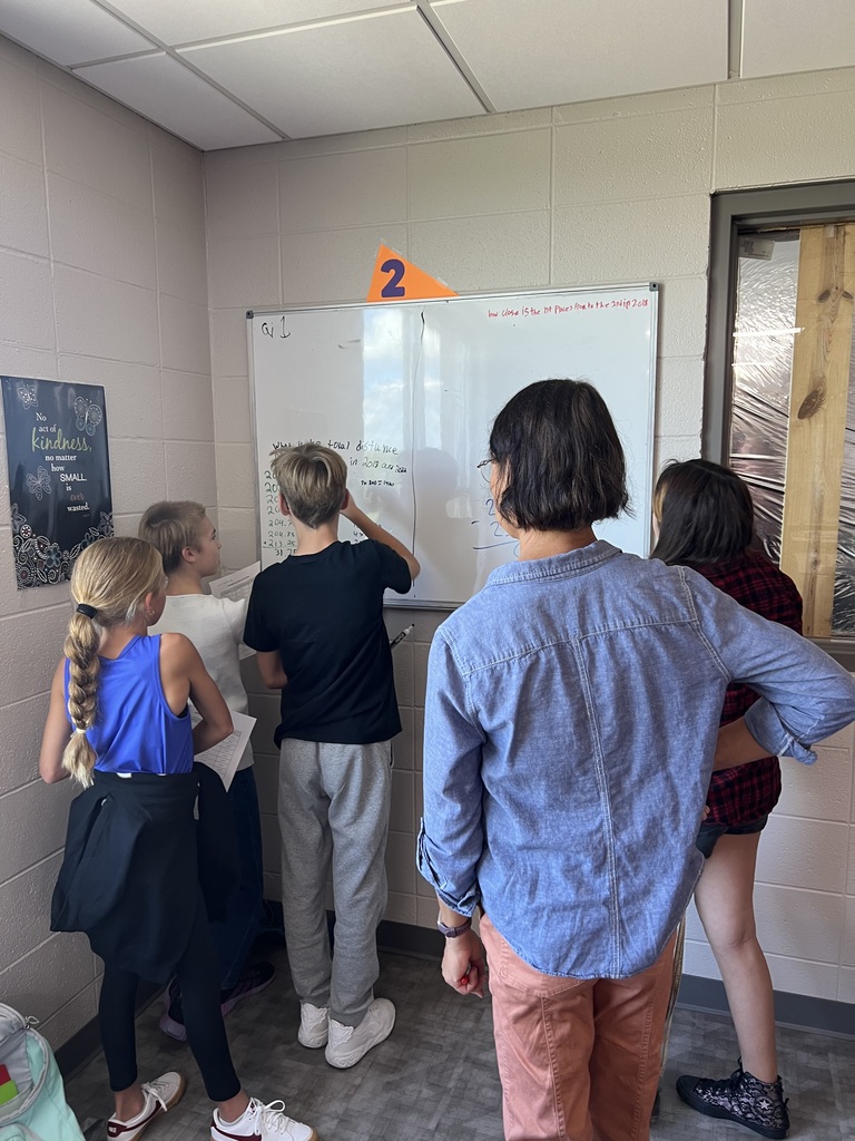 Four middle school students working collaboratively at a vertical non-permanent surface while a teacher looks on.