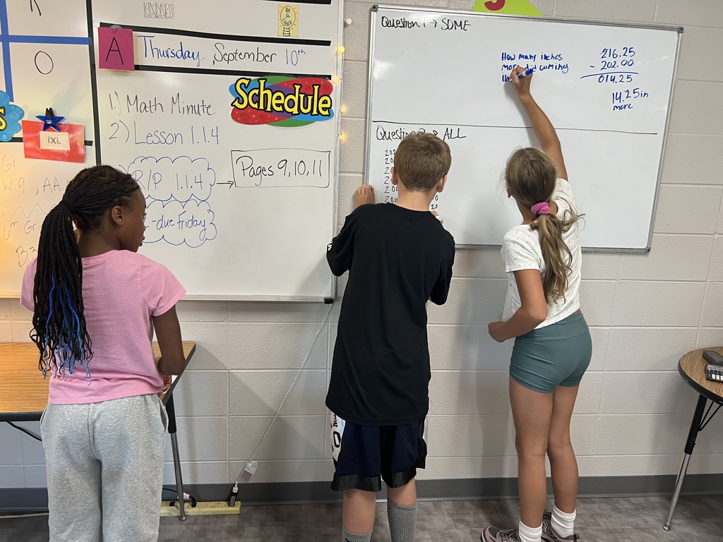 Three middle school students working collaboratiely at a vertical non-permanent surface.