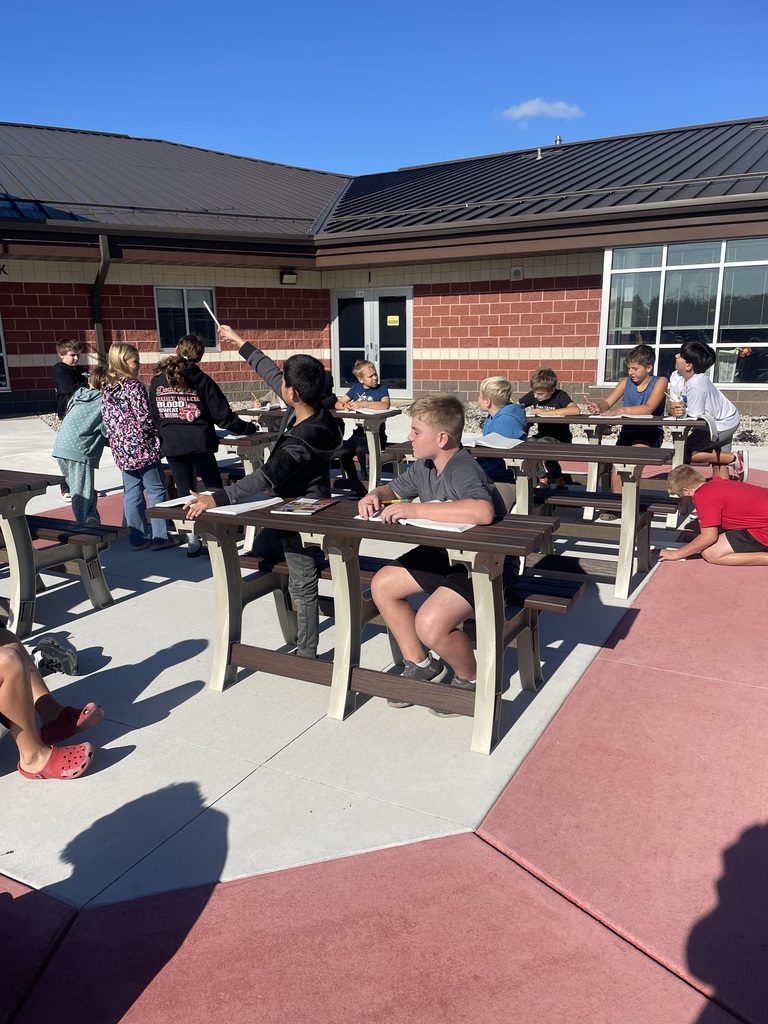 Elementary students sitting at tables at an outdoor learning space.