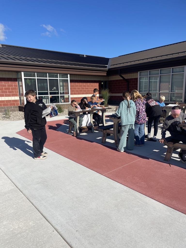 Elementary students sitting at tables at an outdoor learning space.