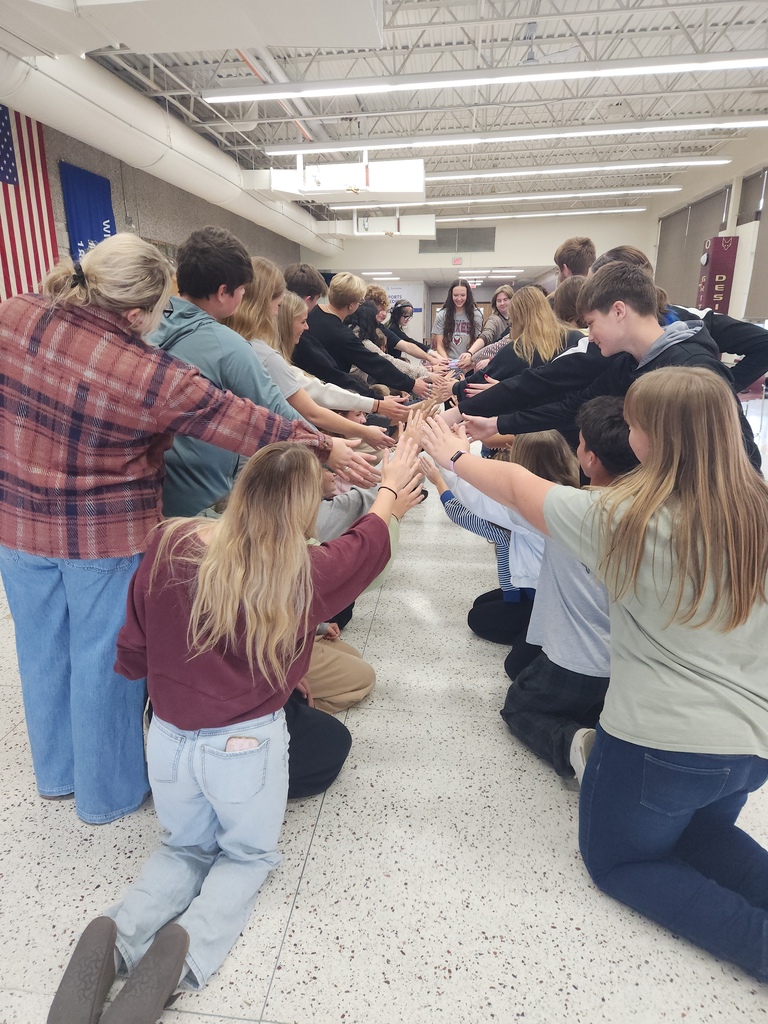 Two lines of people with their inside hand facing in to the middle. One person is at the end, facing all of the hands.