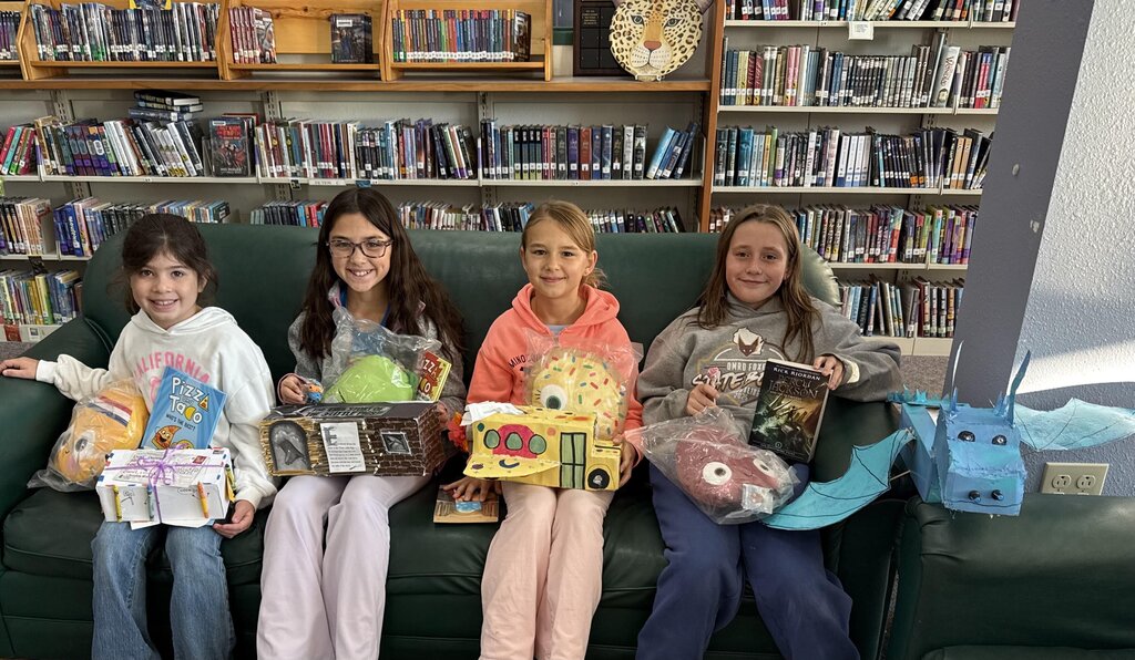 Four elementary students sitting on a couch holding tissue box covers that are book themed.