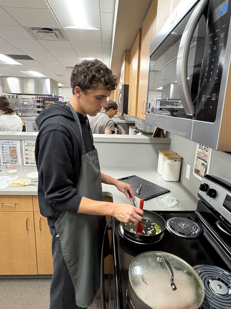 A high school student standing over a stove preparing food.