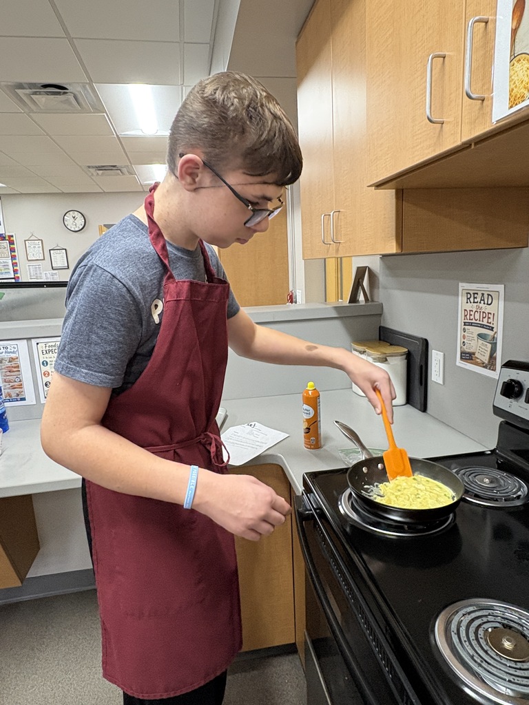 High school student standing over a stove making eggs.