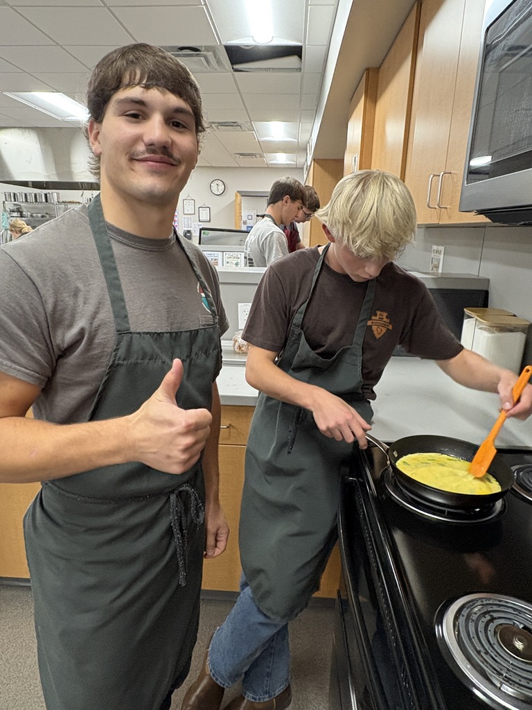 Two high school students standing over a stove making eggs.