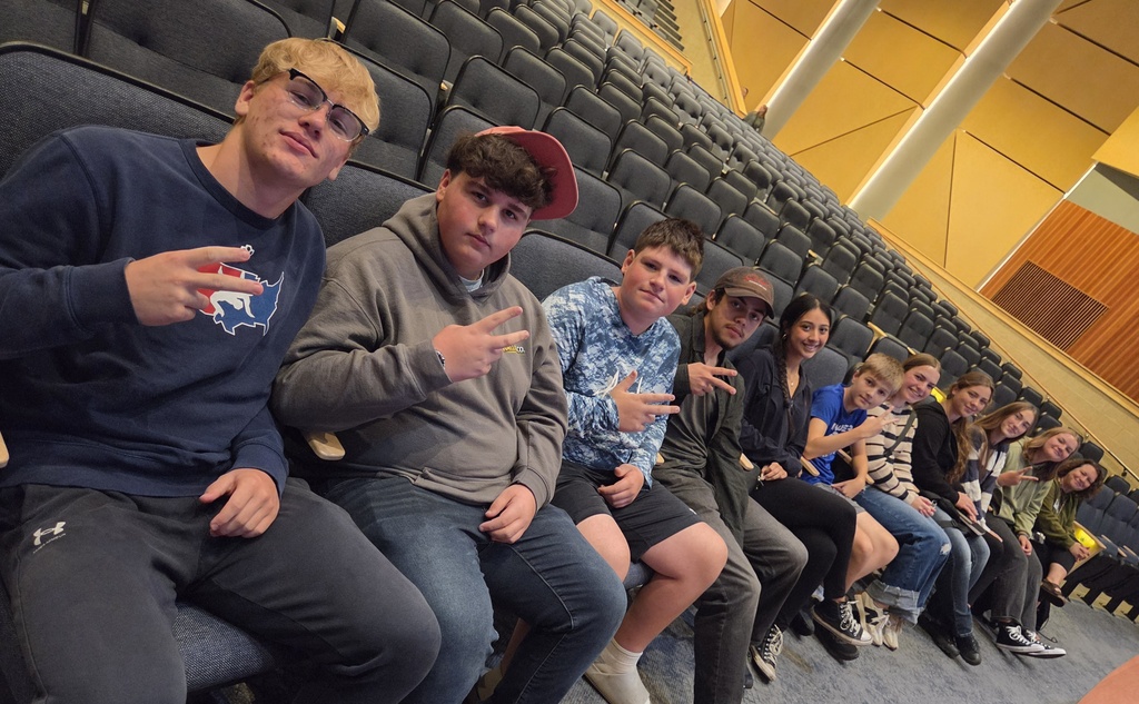 A line of 11 high school students sitting in an auditorium. 