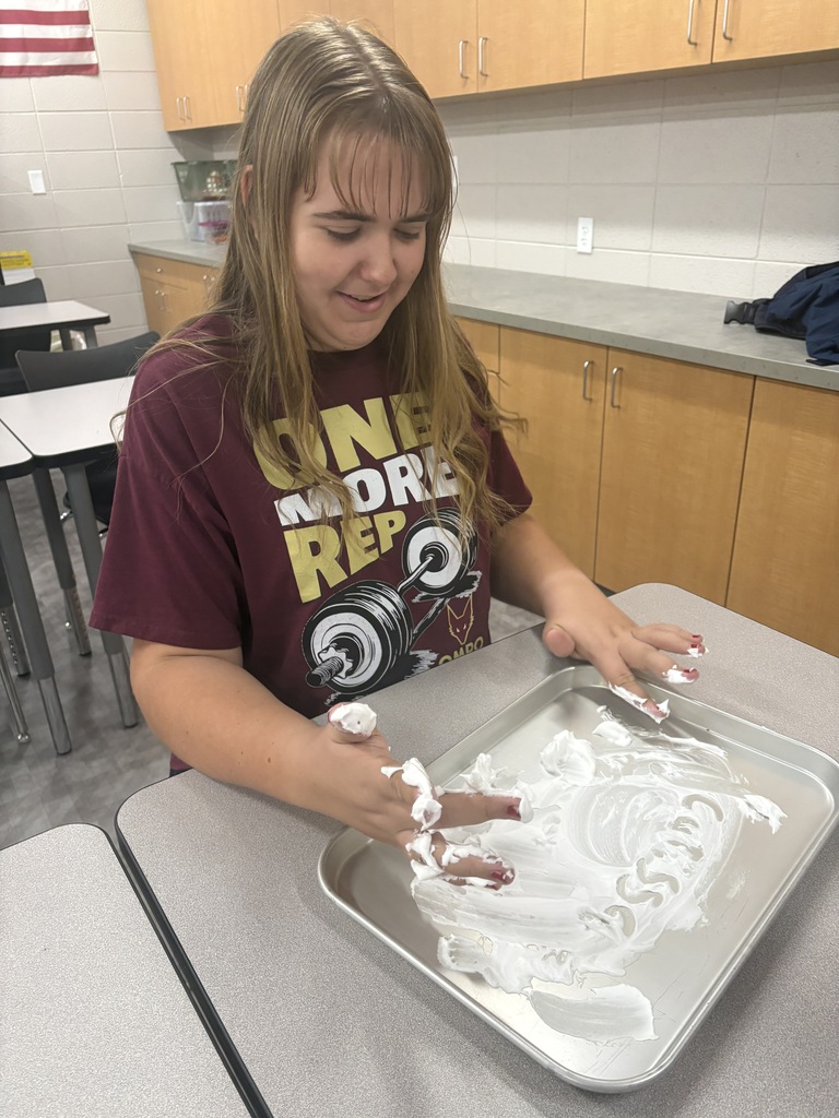 A high school student drawing their name in shaving cream in a tray.