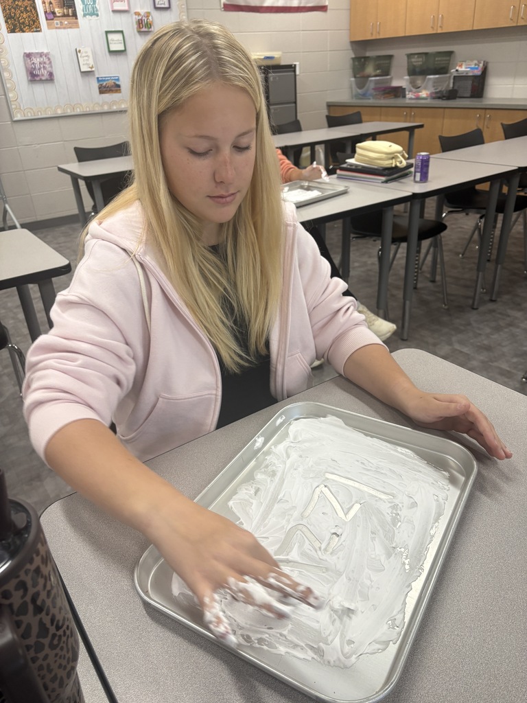 A high school student drawing their name in shaving cream in a tray.