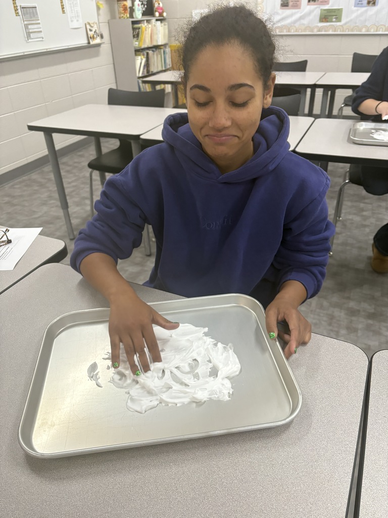 A high school student drawing their name in shaving cream in a tray.