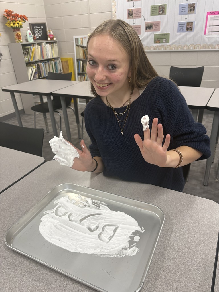 A high school student drawing their name in shaving cream in a tray.