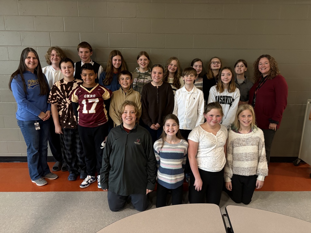 A group of 18 middle school students and two teachers posing in three rows in front of a wall. 