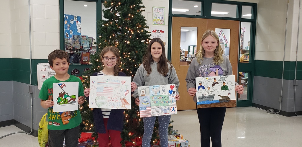 4 students posing in front of a tree holding Veteran's Day posters.