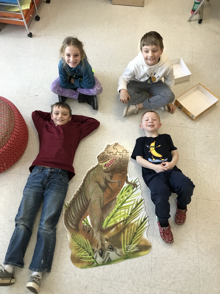 4 elementary students sitting on the floor near a puzzle they built.