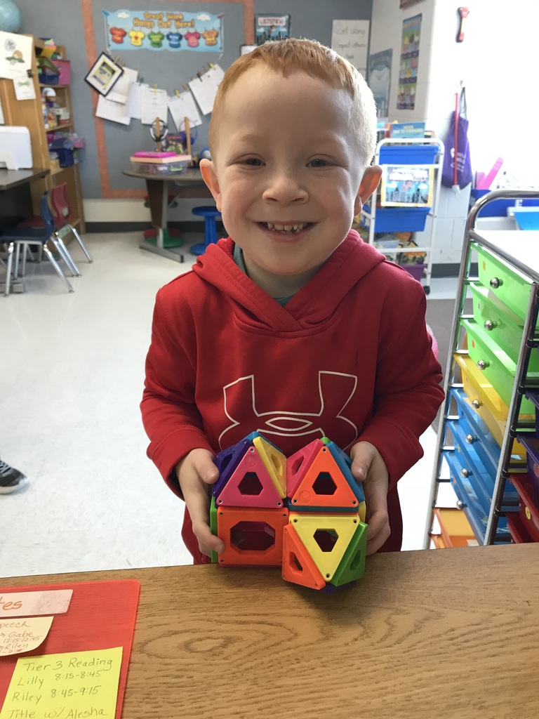Elementary student holding a 3D figure made out of 2D shapes. 