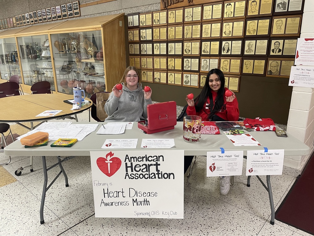 Two high school students sitting at a table with American Heart Association signs and items on it.